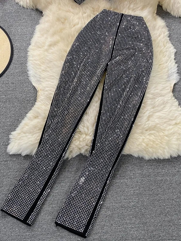 Black straight-leg pants covered in dense silver rhinestones, laid on a white fluffy rug.