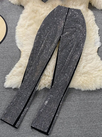 Black straight-leg pants covered in dense silver rhinestones, laid on a white fluffy rug.