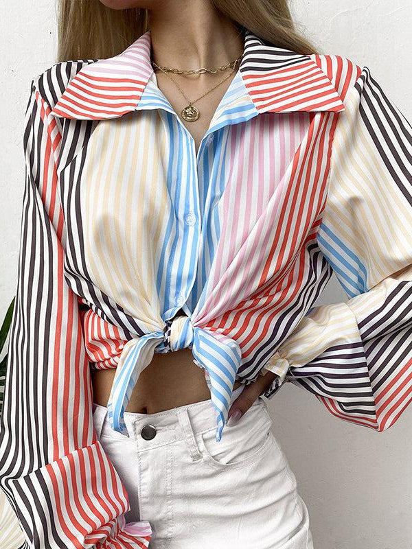 Multicolor striped tie-front blouse with lapel collar and full lantern sleeves, knotted at the waist over white pants.