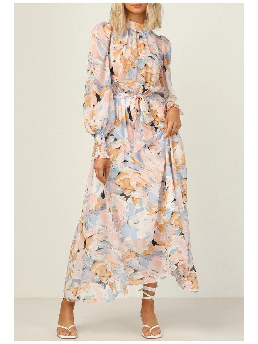 Pastel floral chiffon dress with lantern sleeves, tied waist, flowing maxi skirt, and white strappy sandals.