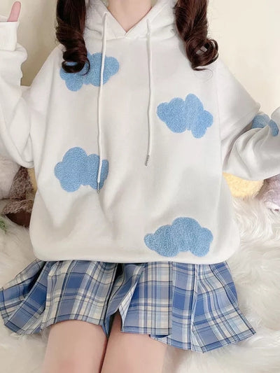 Oversized white hoodie with fuzzy blue cloud patches and drawstrings, paired with a blue plaid pleated skirt.