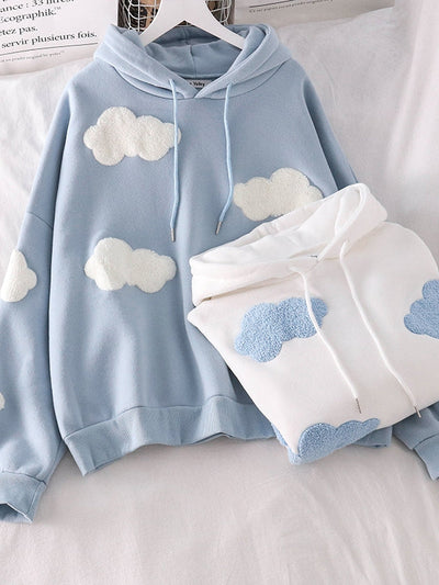 Light blue hoodie with fluffy white cloud patches and a drawstring hood; white hoodie beside it with blue cloud patches.