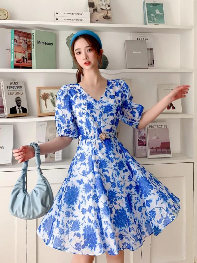 Woman wearing blue and white floral A-line dress with belt and puff sleeves, holding a light blue ruched handbag.