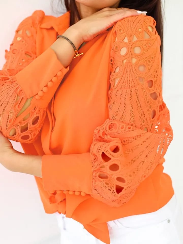 Woman wearing a bright orange oversized shirt with crochet lace sleeves featuring circular cutouts and a solid bodice.