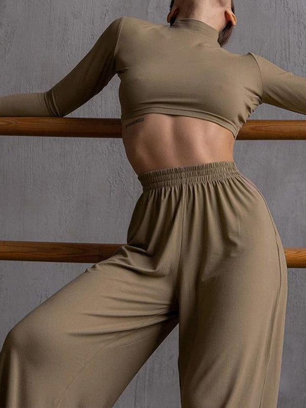 Model in taupe cropped long-sleeve turtleneck top and matching high-waist pants, leaning against a wooden barre.