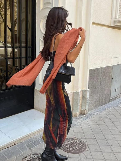 Woman on a city sidewalk wearing a tie-dye mesh tube dress, rust shawl over shoulders, black crossbody bag, ankle boots.