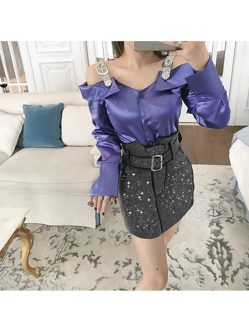 Purple satin off-shoulder top with crystal-embellished straps paired with a black rhinestone mini skirt and a wide belt.