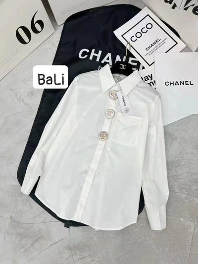 White cotton collared shirt with chest pocket and circular logo buttons, laid on Chanel-branded packaging.