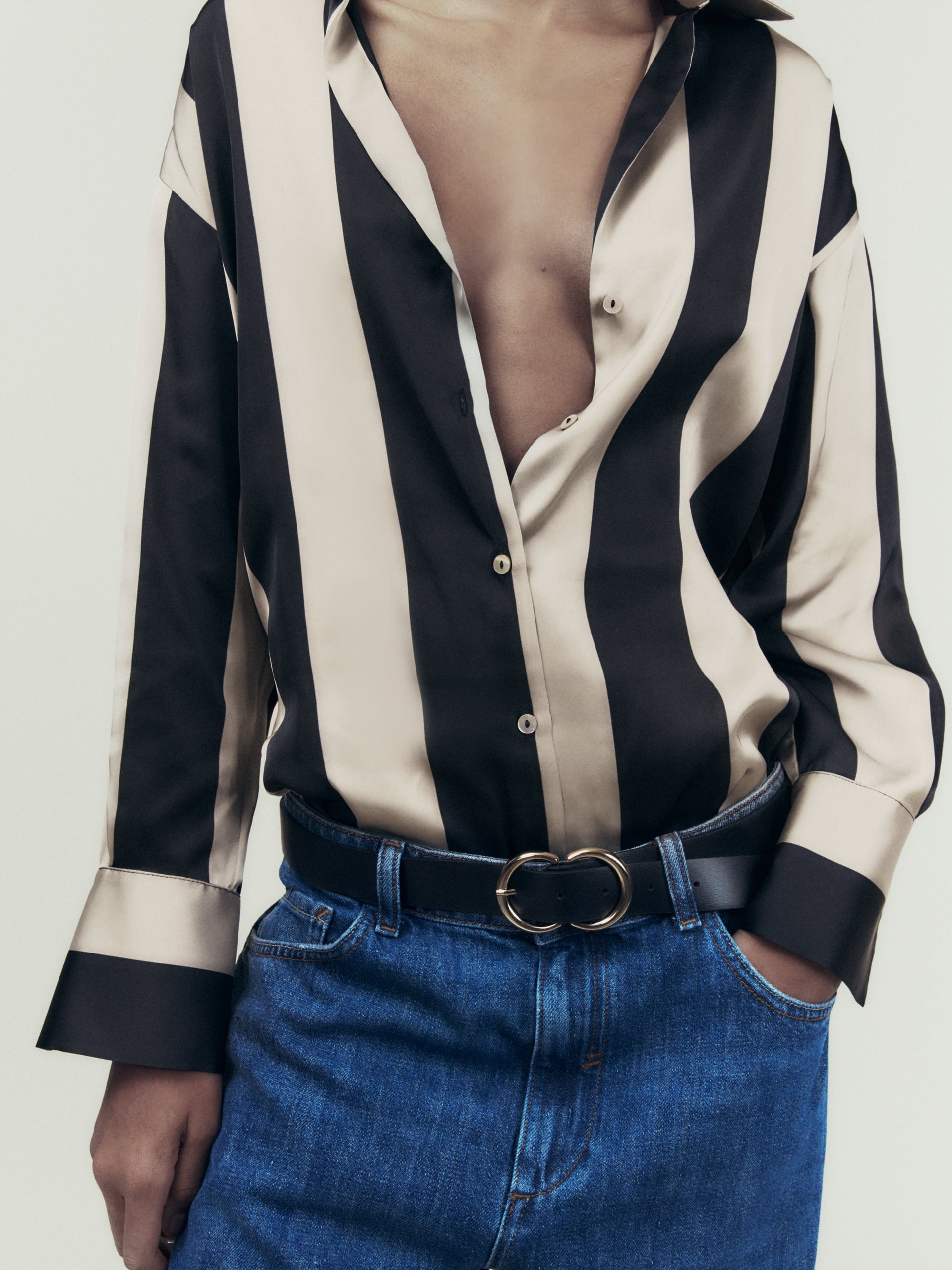Open-front black and beige striped satin shirt with drop shoulders, paired with blue jeans and a black double-ring belt.