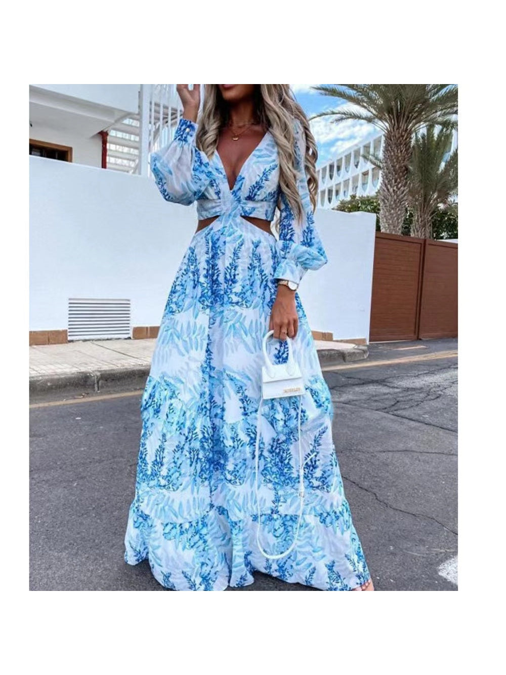 Woman in blue-and-white floral print cutout maxi dress with V-neck, billowy long sleeves, waist cutouts, holding a small white top-handle bag.