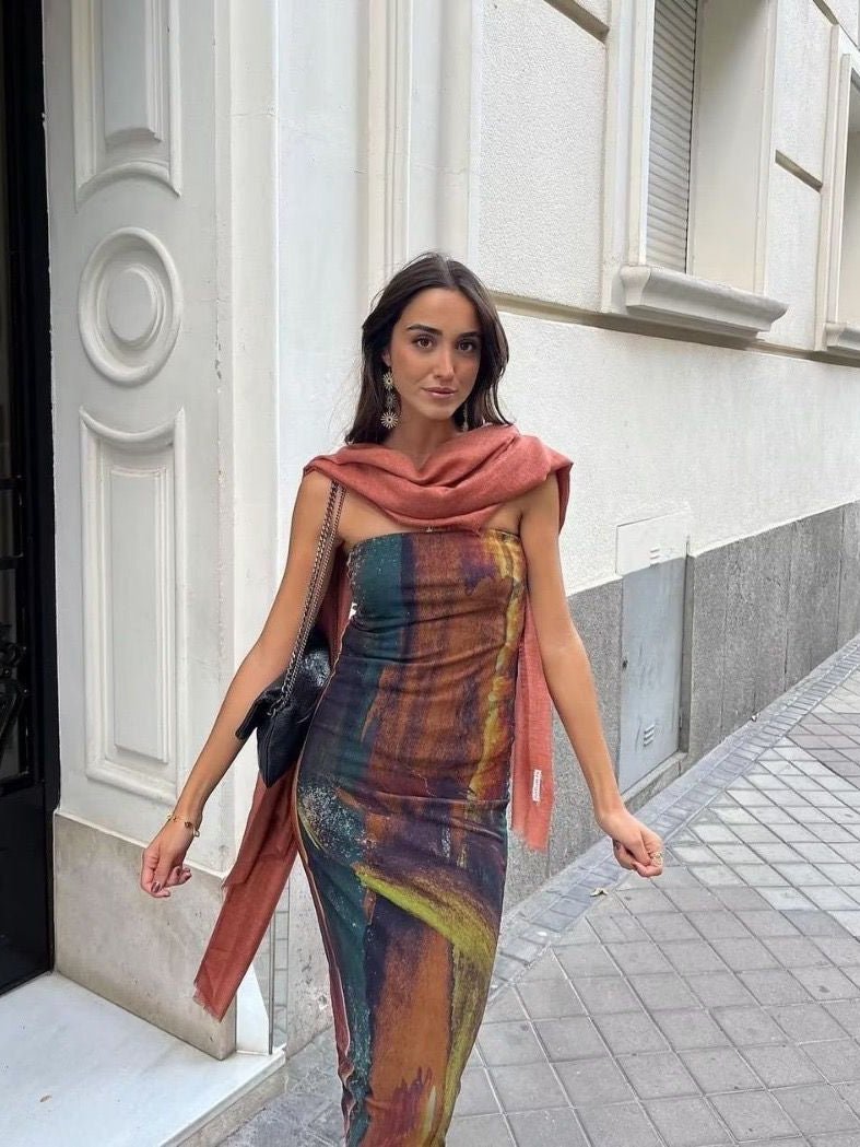 Woman in a multicolor tie-dye mesh tube dress with a rust scarf draped over shoulders, carrying a black chain-strap bag.
