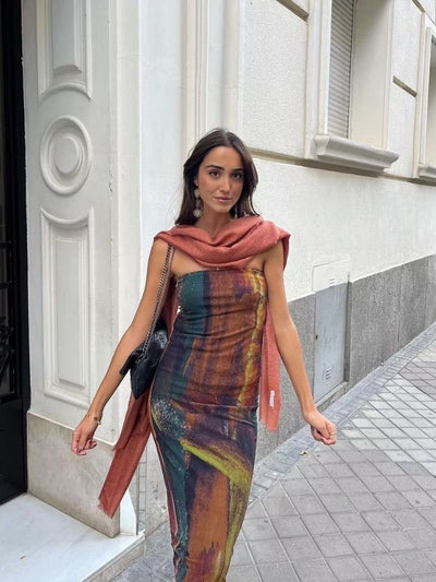 Woman in a multicolor tie-dye mesh tube dress with a rust scarf draped over shoulders, carrying a black chain-strap bag.