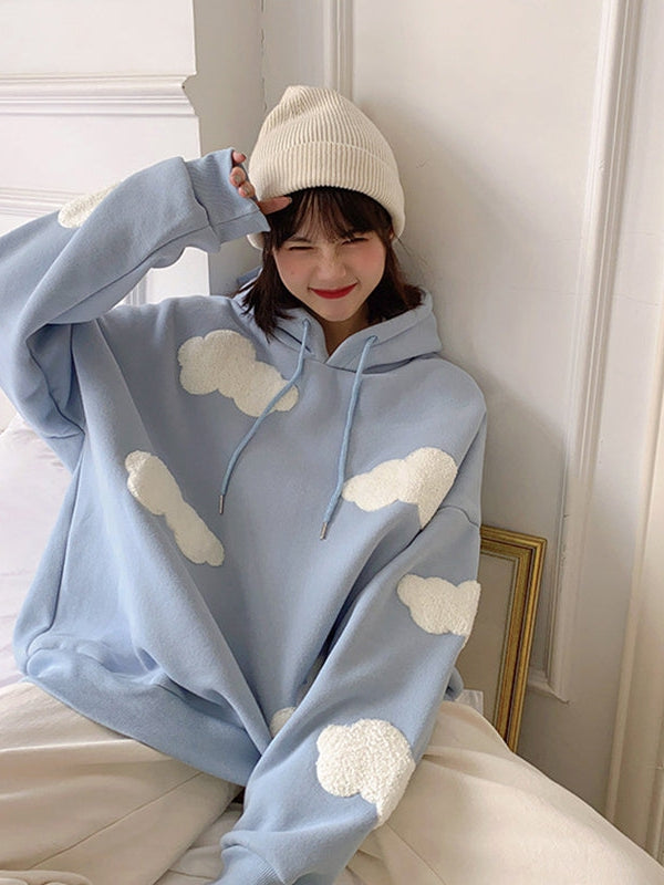 Light blue oversized hoodie with white fluffy cloud patches, drawstrings, worn by smiling young woman in beige beanie.