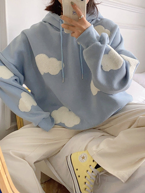 Oversized light-blue hoodie with white cloud patches on sleeves and chest, blue drawstrings, worn with beige pants.