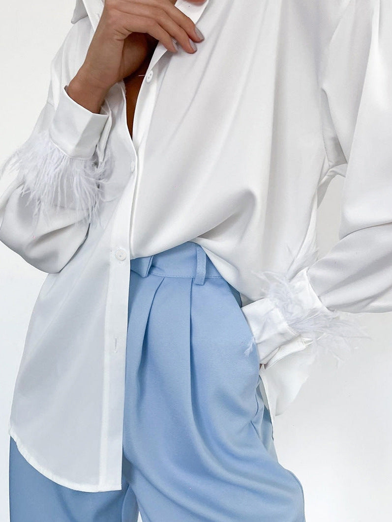 White satin shirt with feather cuffs, paired with light blue pleated trousers.