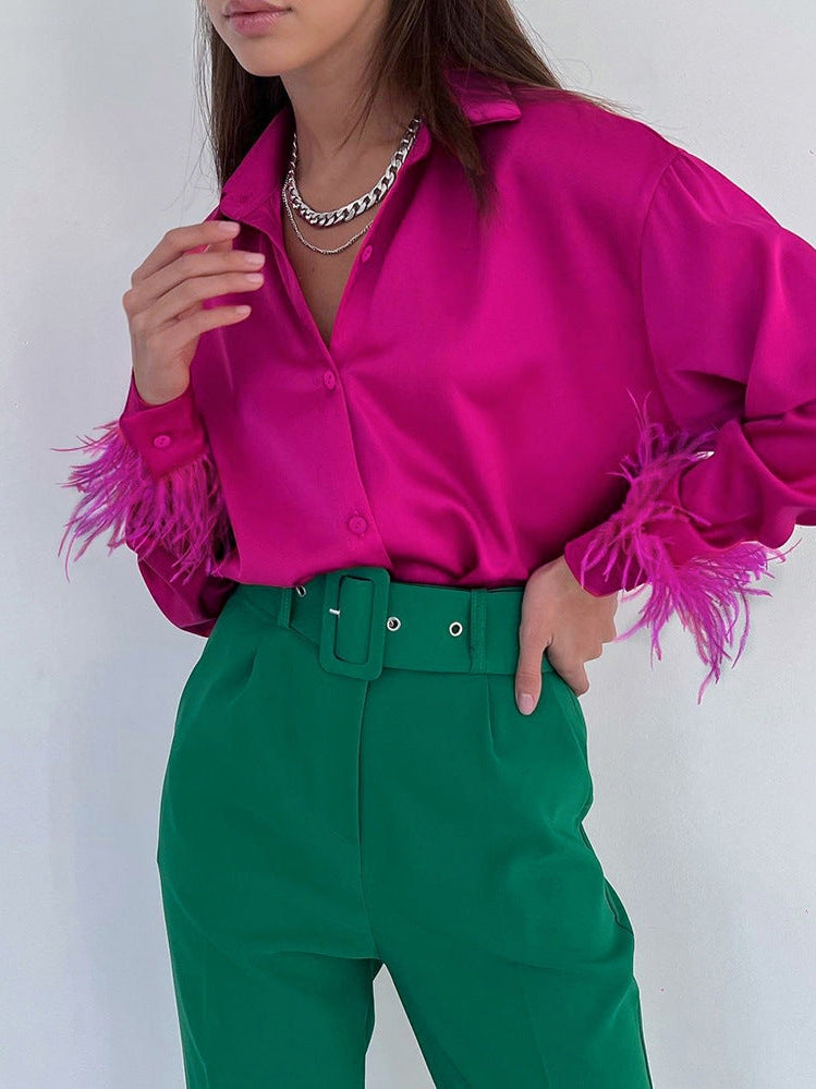 Magenta satin button-down shirt with pink feathered cuffs, worn with green high-waisted pants and a wide belt.