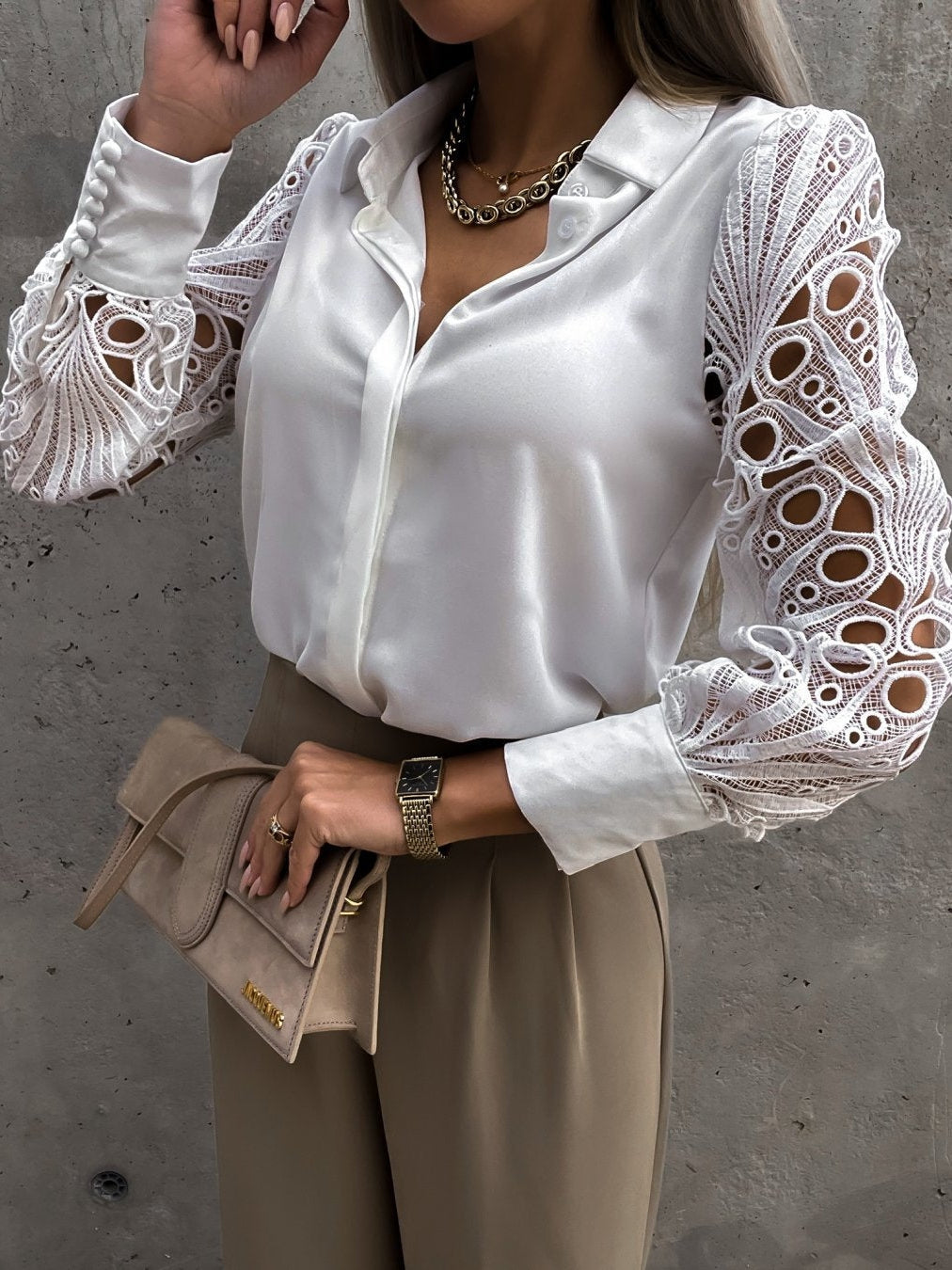 White satin oversized crochet hollow-out shirt with lace sleeves, paired with beige trousers and a beige clutch.