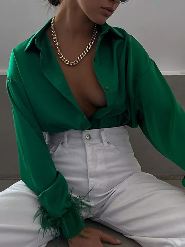 Green satin shirt with feathered cuffs, high-waisted white pants, gold chunky chain necklace, model posing.