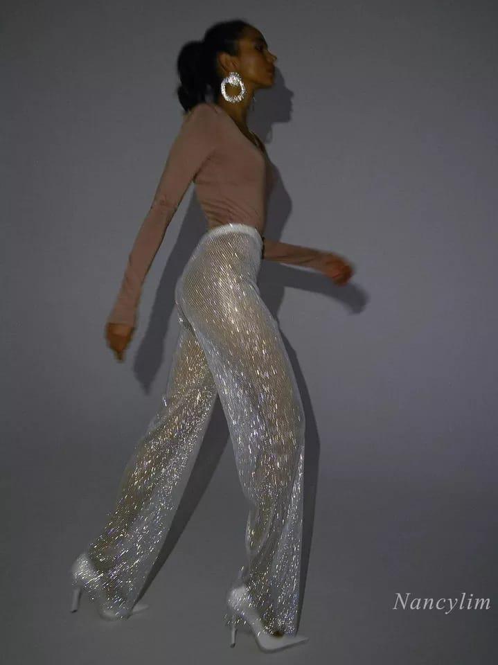 Side-profile of a model in blush top wearing glittery silver sequin pants, white heels, and large hoop earrings.