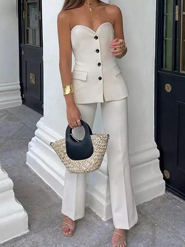 White corset-style strapless tube top with black buttons, ivory wide-leg pants; woven straw tote with black handle.